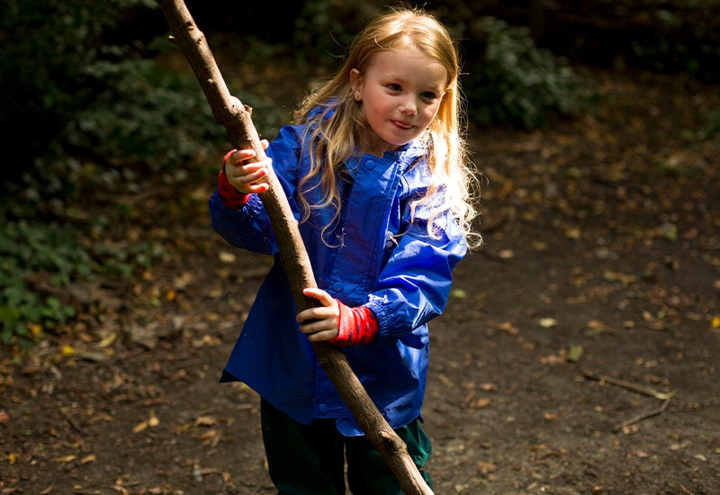 blonde girl holding a long stick, wearing vibrant blue muddy puddles waterproof jacket