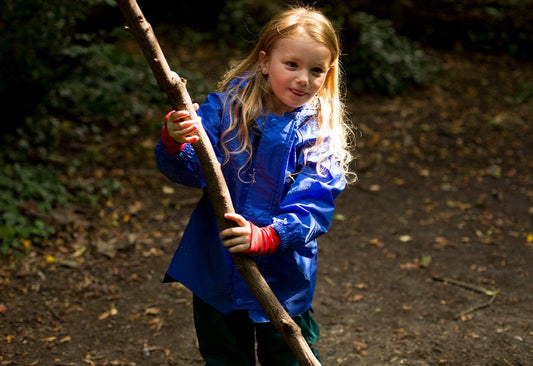 blonde girl holding a long stick, wearing vibrant blue muddy puddles waterproof jacket