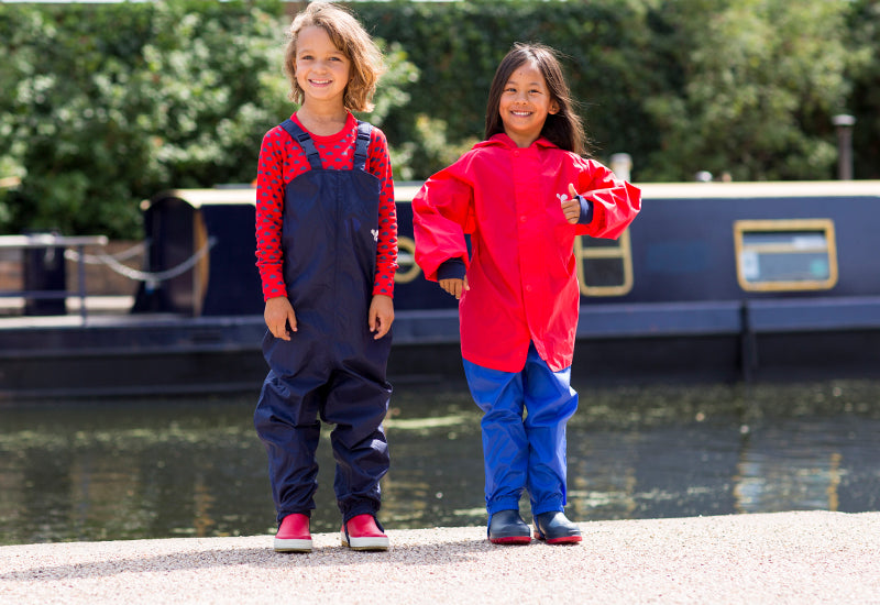 boy and girl standing by canal, wearing vibrant muddy puddles waterproof dungarees, jacket and trousers