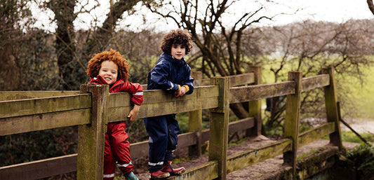 two boys stood on bridge wearing muddy puddles red and navy puddle suits