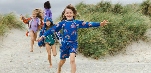 Children in colorful waterproof swimwear running on a sandy beach with grassy dunes