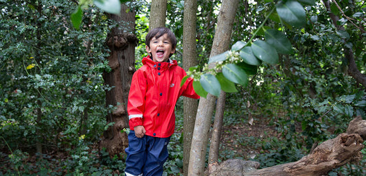 Smiling child in red waterproof jacket and navy rain pants playing outdoors in a forest