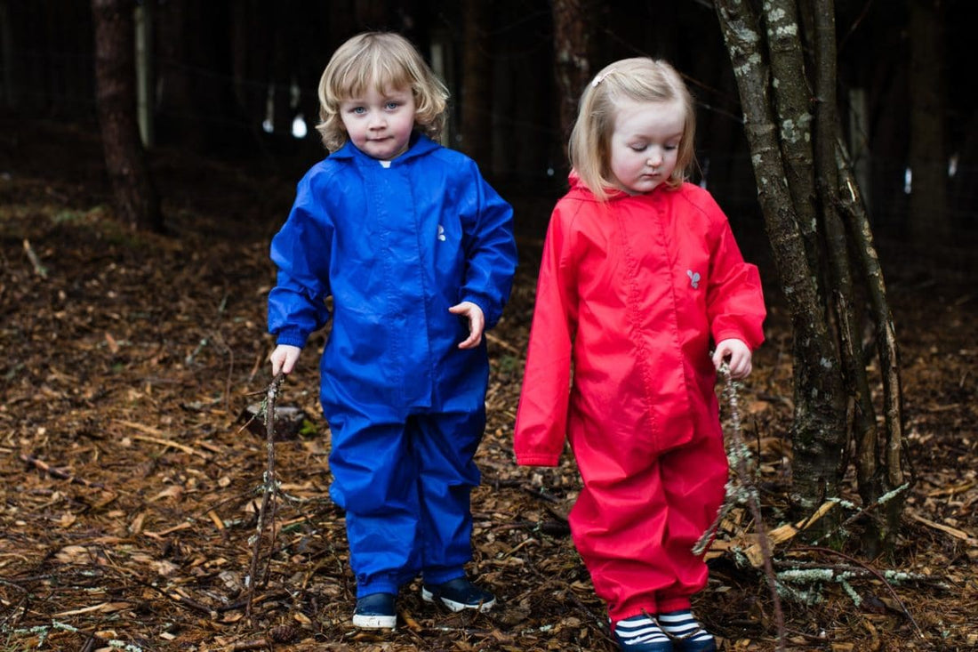 children stood in woodland area, wearing vibrant muddy puddles puddlesuits