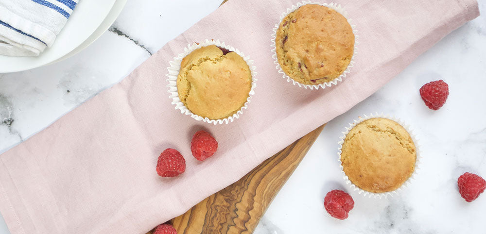 Fresh raspberry muffins on a pink cloth with loose raspberries, marble background