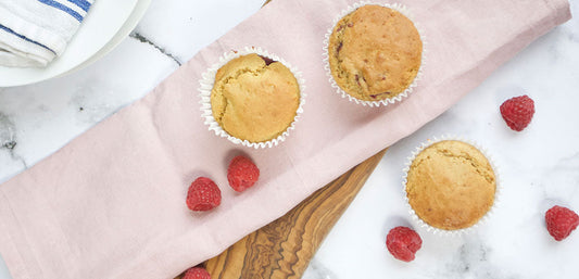 Fresh raspberry muffins on a pink cloth with loose raspberries, marble background