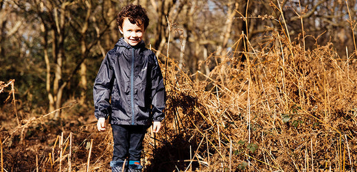 Child wearing waterproof jacket and boots outdoors in a forest with dry grass