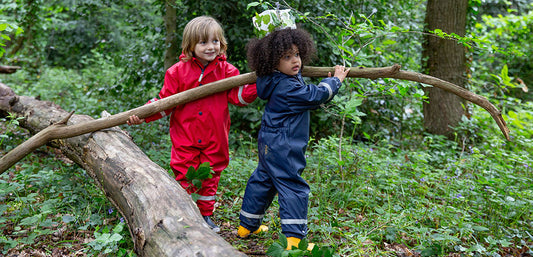 boys standing in woodland holding tree branch, wearing red and navy mussy puddles waterproofs