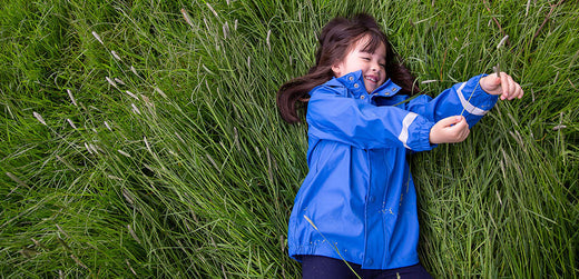 Child in blue waterproof jacket lying on grass, outdoor kids rainwear clothing