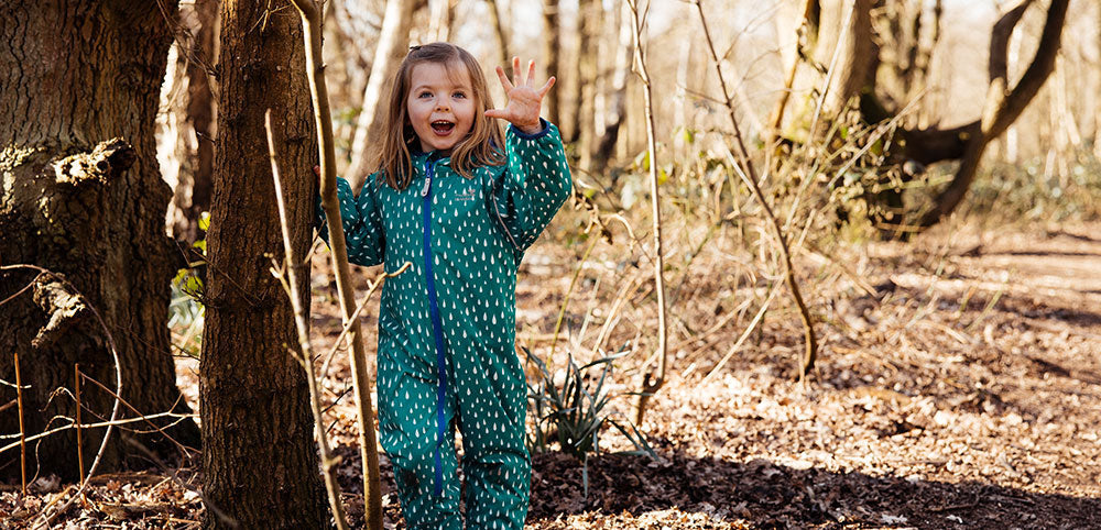Child in green waterproof puddle suit playing outdoors in a woodland setting