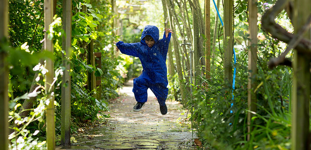 boy jumping in rain wearing blue muddy puddles puddle suit