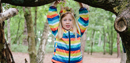 Child in rainbow striped waterproof jacket playing outdoors in a forest