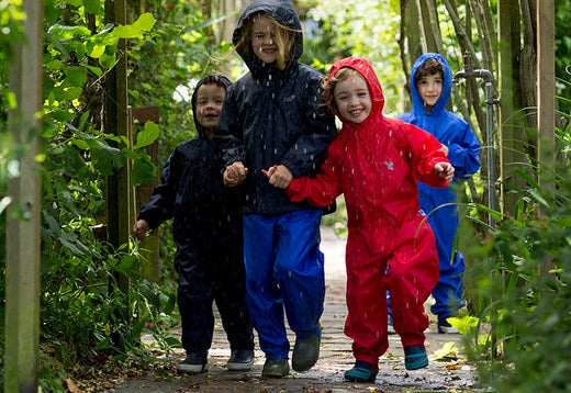 children holding hands and running through rain wearing colourful muddy puddles waterproofs