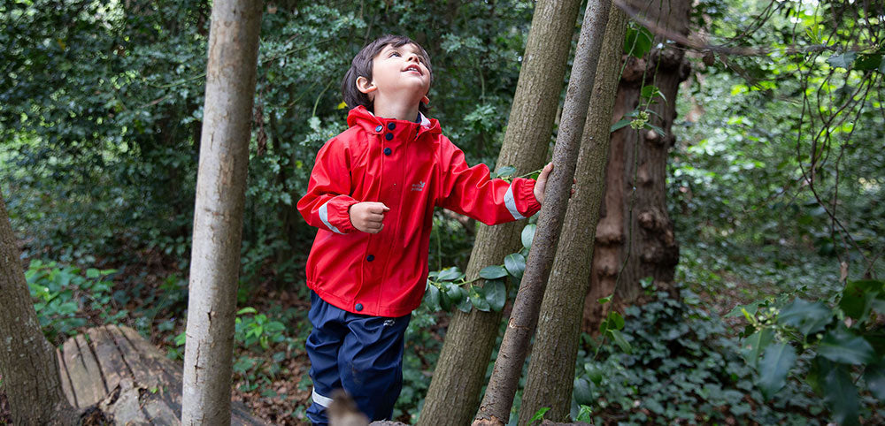 Child in red waterproof jacket exploring a forest, kids outdoor rainwear for woodland adventures
