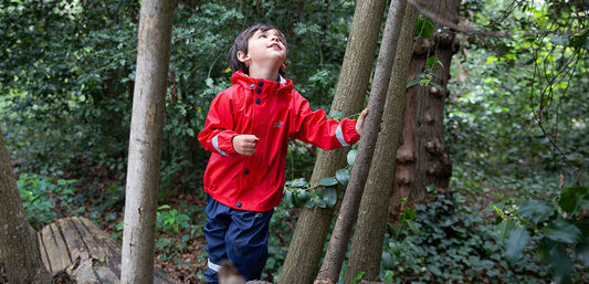 Child in red waterproof jacket exploring a forest, kids outdoor rainwear for woodland adventures