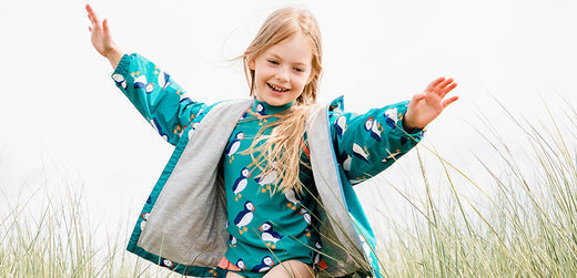 Smiling child wearing a puffin print waterproof jacket outdoors in tall grass