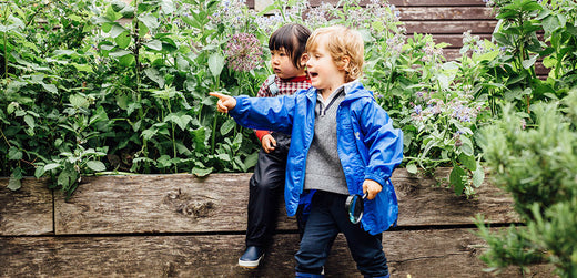 boy and girl in a garden wearing muddy puddles waterproofs, boy is pointing at something in the distance