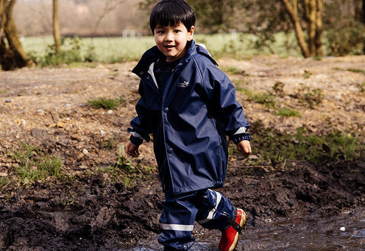 boy walking through muddy puddle in woodland, wearing muddy puddles navy waterproof jacket and trousers