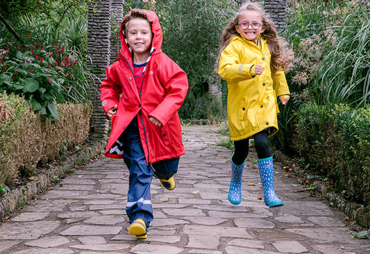 boy and girl running through garden, wearing vibrant muddy puddles waterproof jackets, trousers and wellies