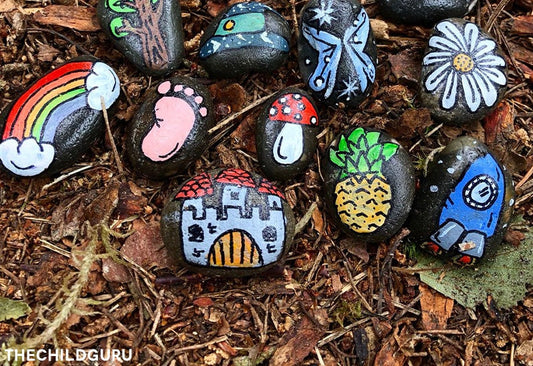 black pebbles painted by children with colourful designs, on a forest floor