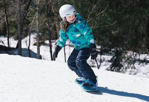 girl snowboarding on ski slope, wearing muddy puddles skiwear