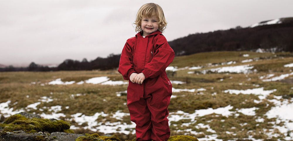 Smiling child snood on snowy field wearing red muddy puddles puddlesuit