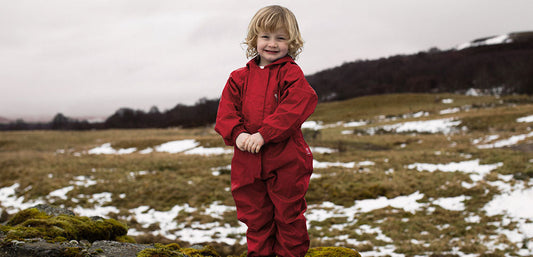 Smiling child snood on snowy field wearing red muddy puddles puddlesuit