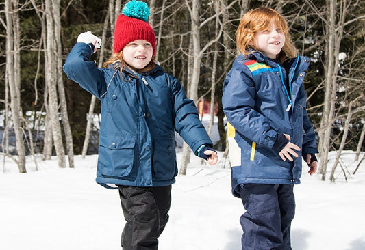 children standing in snow throwing snowballs, wearing navy muddy puddles ski jackets