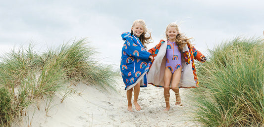 Two children in colorful waterproof jackets with rainbow patterns running on a sandy beach