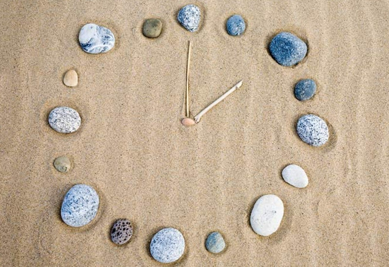 pebbles and sticks arranged like a clock face on a bed of sand