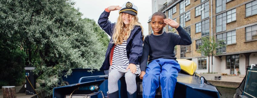 boy and girl sitting on canal boat saluting to the camera, girl is wearing captain's hat 