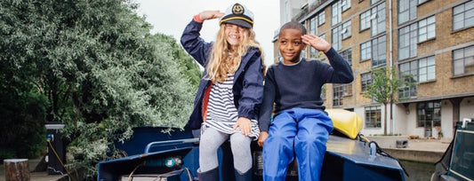 boy and girl sitting on canal boat saluting to the camera, girl is wearing captain's hat 