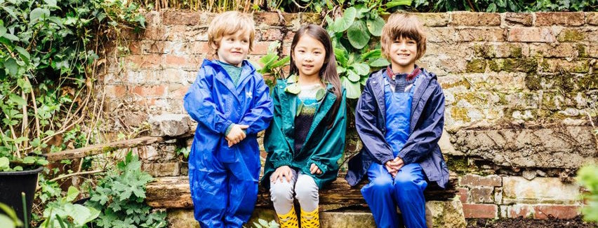 children sitting on bench in garden, wearing blue and green muddy puddles originals waterproofs