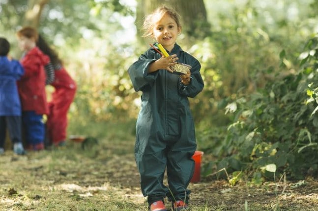 girl at forest school holding a mud pie wearing green muddy puddles puddlesuit