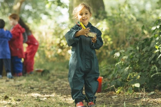 girl at forest school holding a mud pie wearing green muddy puddles puddlesuit