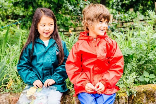 boy and girl sitting on garden wall wearing vibrant red and green muddy puddles waterproof jackets