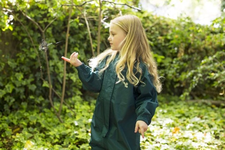 girl stood in garden, surrounded by ivy, looking at a spider web, wearing green muddy puddles puddlesuit