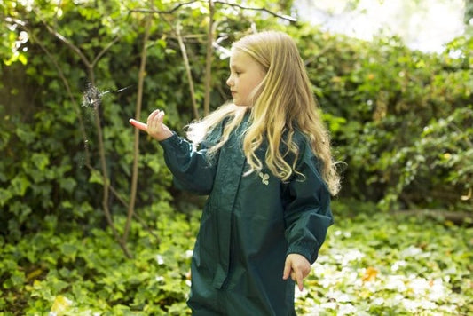 girl stood in garden, surrounded by ivy, looking at a spider web, wearing green muddy puddles puddlesuit