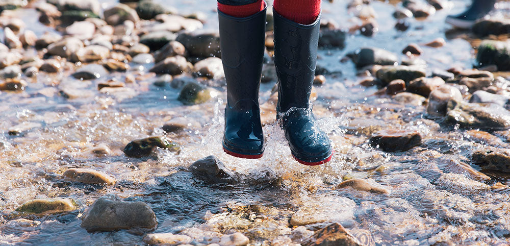 child jumping in sea wearing muddy puddles navy classic wellies