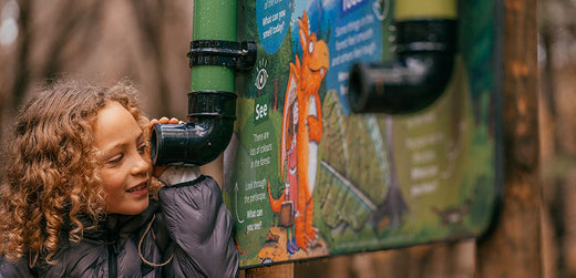 Child in waterproof jacket playing at outdoor learning board in nature
