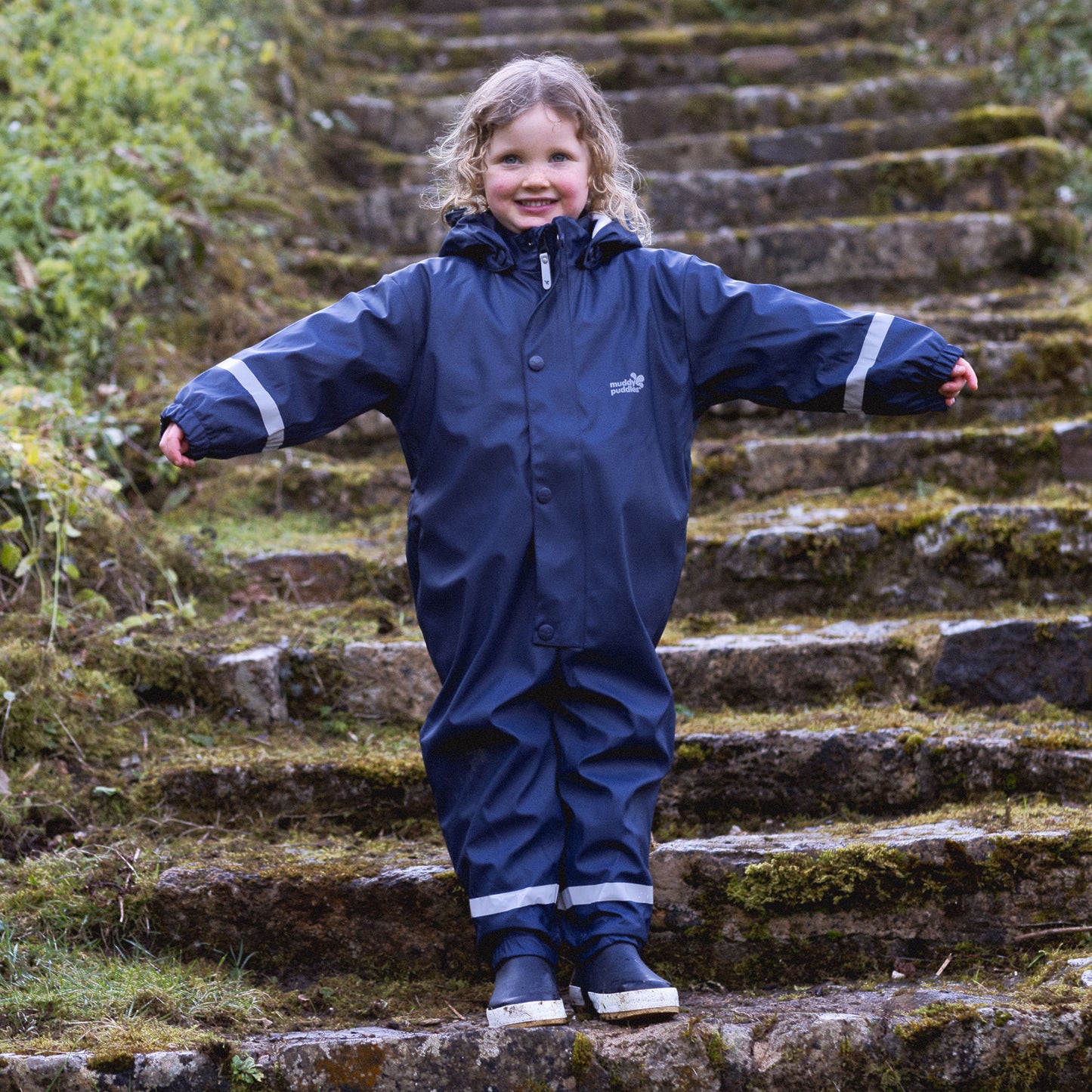 a child wearing a puddleflex waterproof puddle suit going down some outdoor stairs