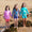 Three girls in UV Protective Surf Sets Multi Check, starfish and ice cream designs stand on a beach holding hands, smiling at the camera.