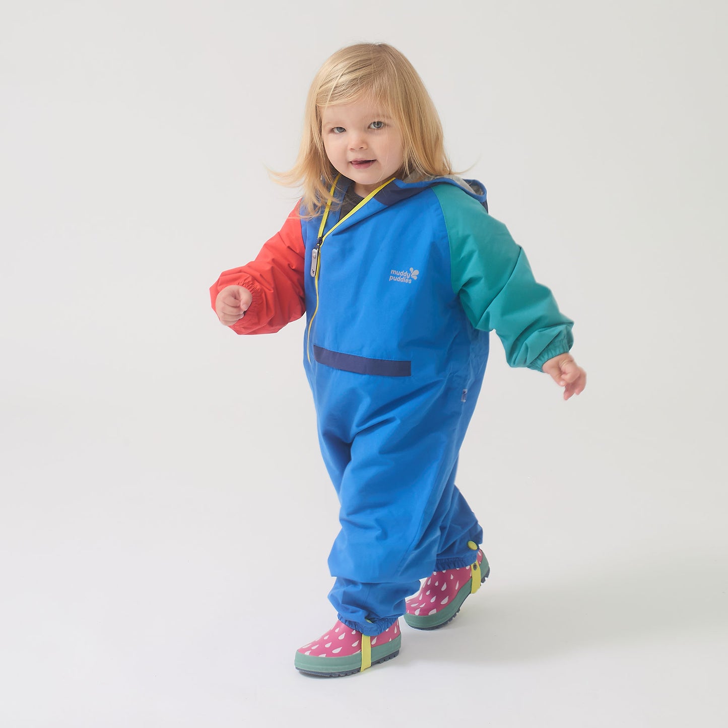 Toddler wearing the EcoLight Lightweight Waterproof Puddle Suit Blue Colourblock, exploring in colorful rain boots; durable, waterproof design ideal for active play in wet weather.
