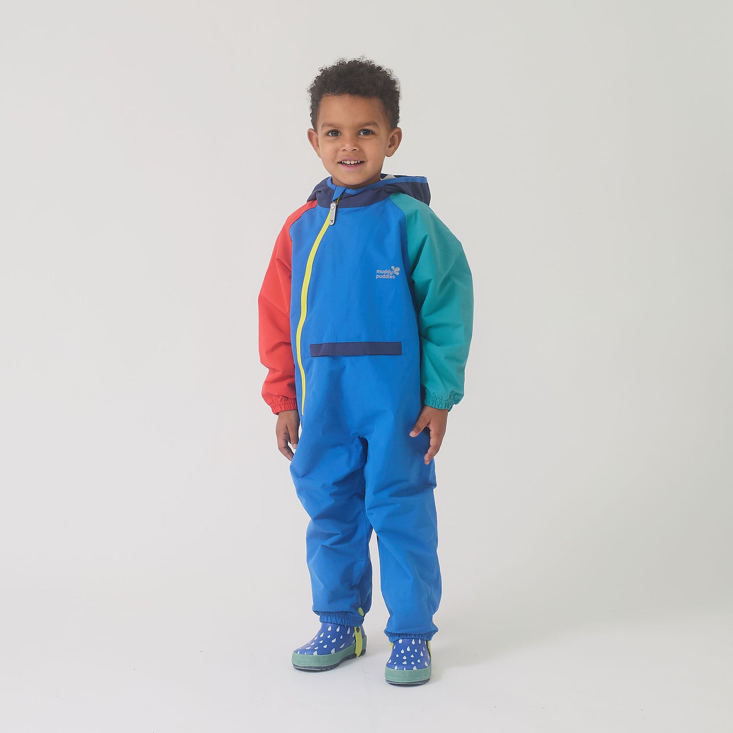 Child in EcoLight Lightweight Waterproof Puddle Suit Blue Colourblock, smiling, showcasing durable, waterproof design with hood and elasticated cuffs, ideal for rainy-day play.
