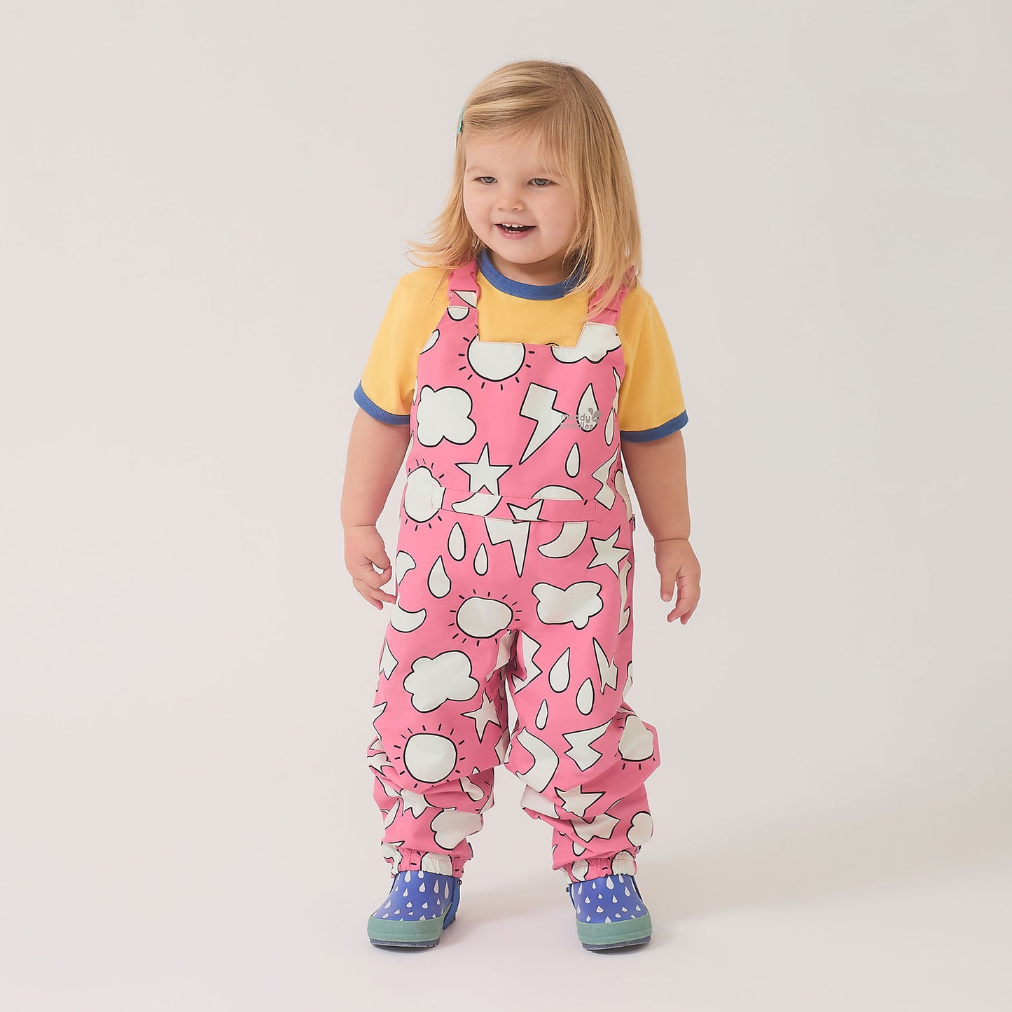 Toddler in EcoLight Waterproof Dungarees Pink Weather, featuring playful weather prints, adjustable straps, and waterproof design, paired with blue rain boots for outdoor adventures.