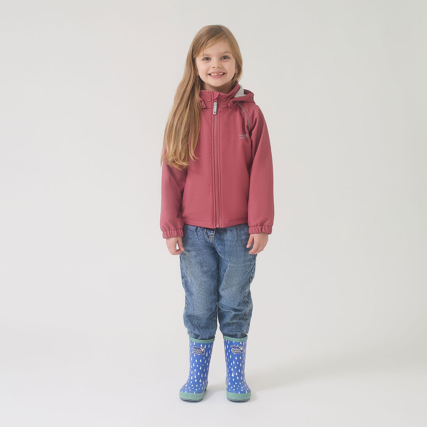 Young girl in a Waterproof Softshell Jacket Pink with blue jeans and raindrop-printed boots, showcasing durable, high-performance outdoor wear.