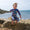 A young boy joyfully leaps off rocks at the beach, wearing a UV Protective Surf Suit Multi Check.